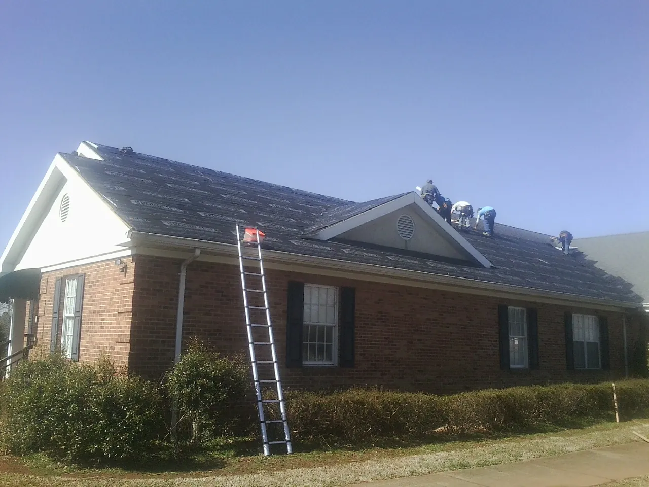 Crew tearing shingles off a brick ranch roof with a ladder set — Emergency Roof Repair work by our crew in Toccoa