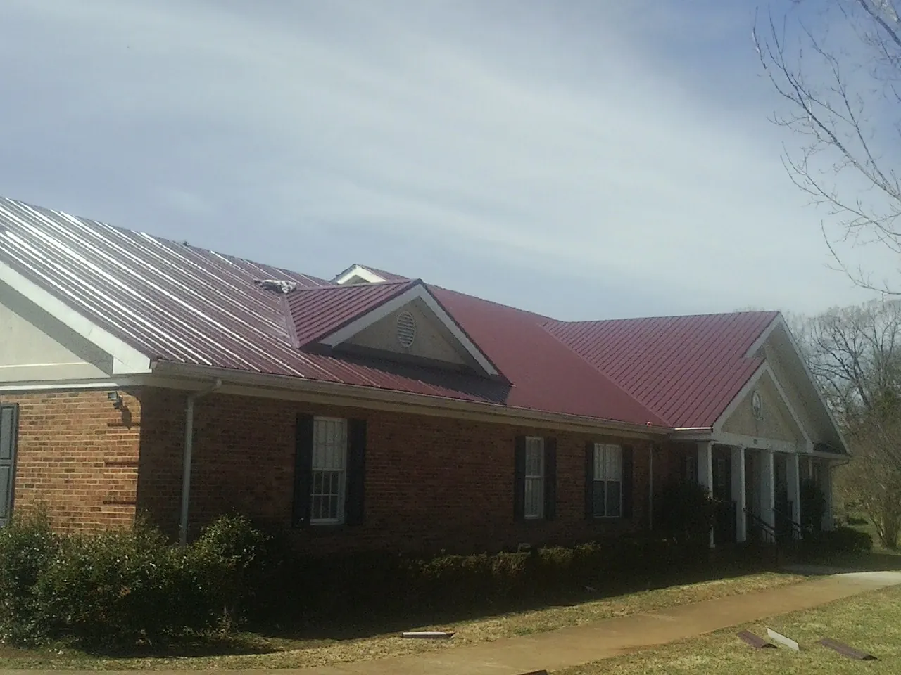 Red metal roof with gabled entries on a long brick building, from a Hail Damage Roof Repair job in Toccoa